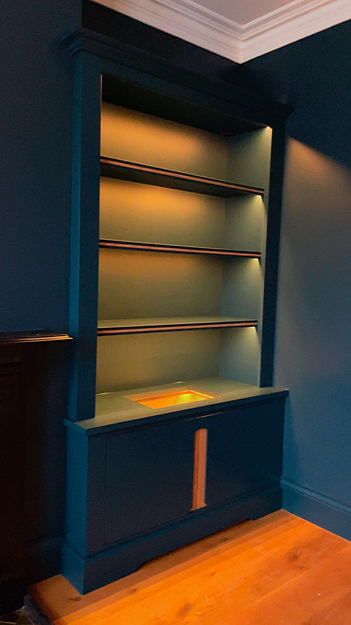 Deep blue display cabinet with illuminated open shelves and oak pull